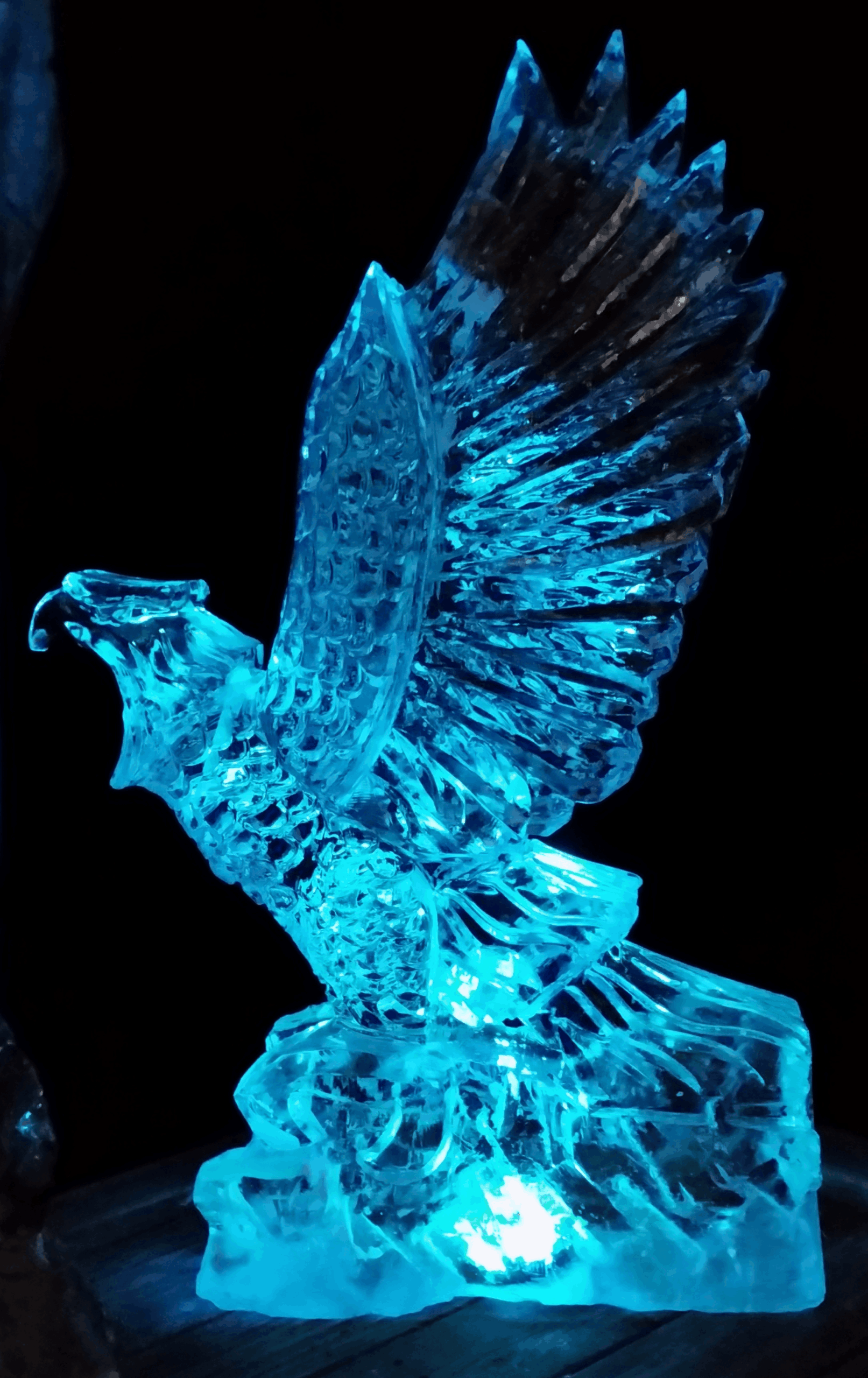 Stunning clear ice sculpture of an eagle with wide spread wings lit in blue