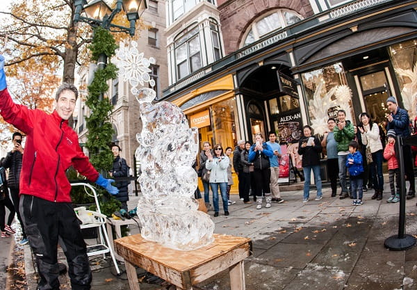 People walking past detailed ice carvings displayed along a town promenade