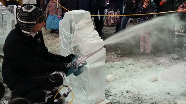 Close up of an ice sculptor chiseling and spraying water onto a winter installation