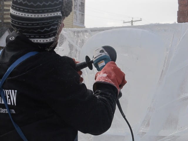 Artisan using a specialized grinding power tool to shape a block of ice