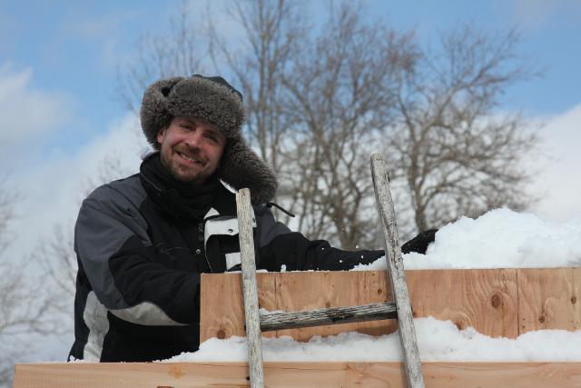 Man in a winter beanie working on a wooden frame setup outdoors