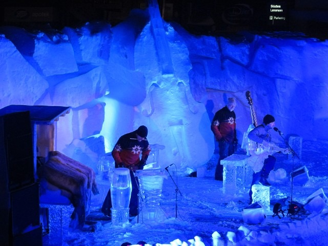 Production crew moving equipment setups through a brilliant blue illuminated ice tunnel
