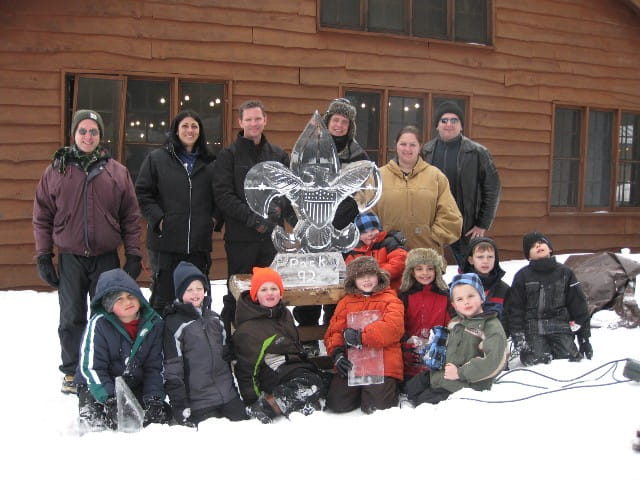 Group of festival attendees posing outdoors in front of a log cabin building