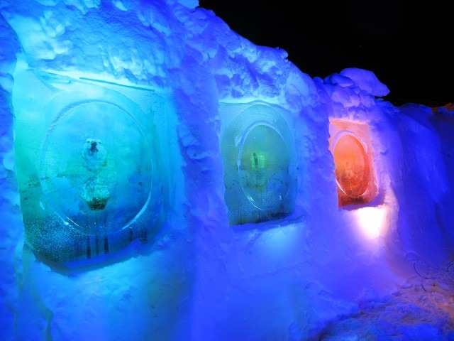 Vibrant green and blue architectural windows carved directly into a thick snow wall