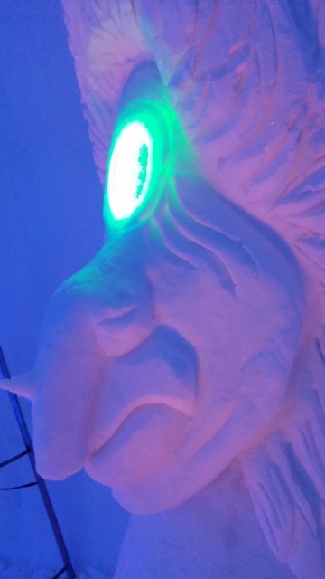 Close up of a sculpted ice face with a glowing green eye element