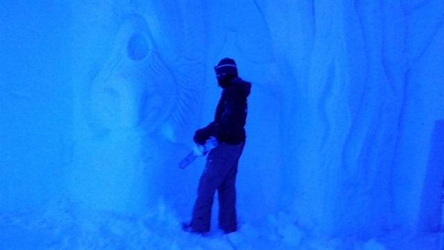 Worker silhouette sculpting an ice wall during a winter installation
