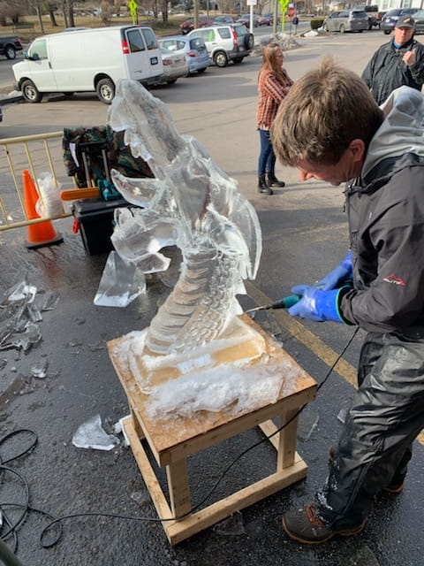 Artisan putting final touches on a detailed ice sculpture block on a sidewalk