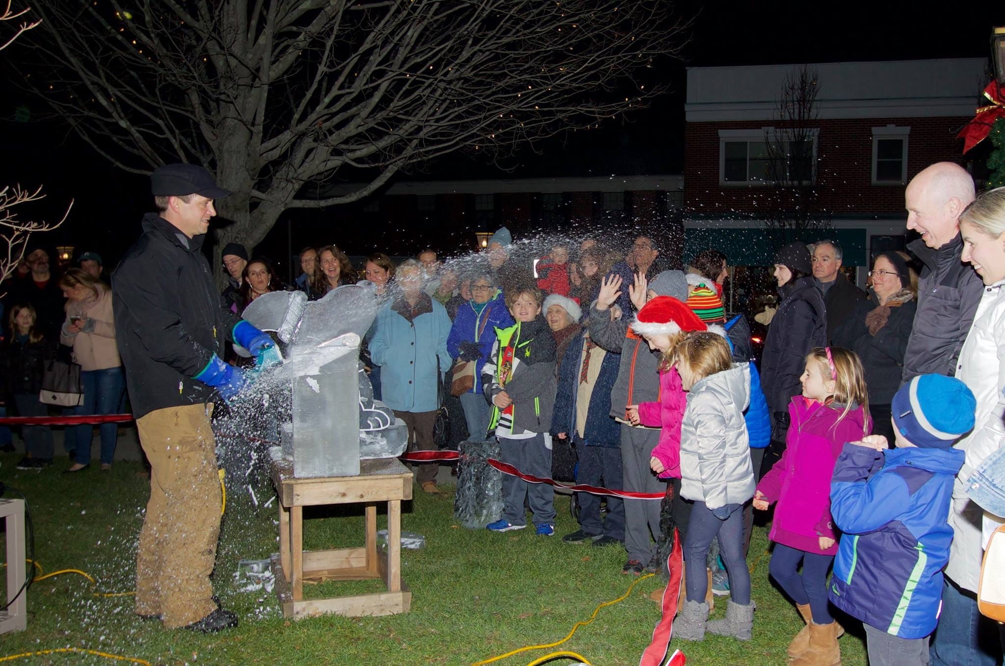 Evening community festival crowd gathering around a lit outdoor ice carving stage