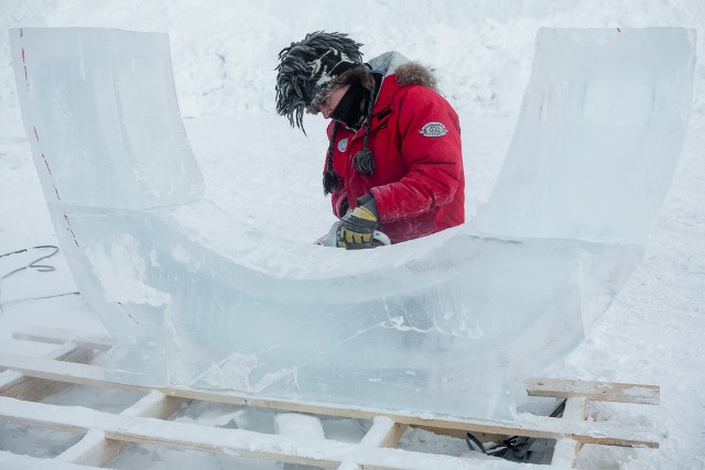 Ice carver in a red parka working on a snow sculpture mound outdoors
