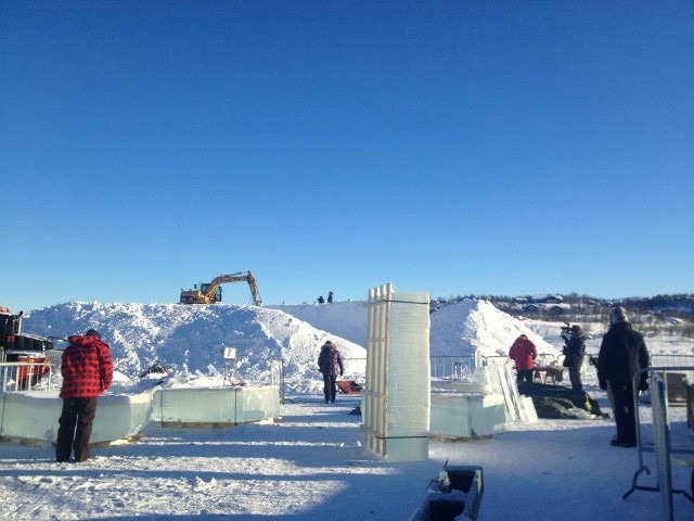 Construction machinery moving massive blocks of clear ice across a snowy field