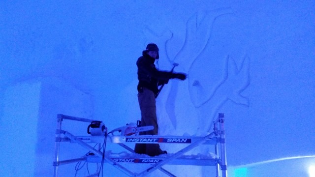 Sculptor detailing a large blue-lit ice mural at night