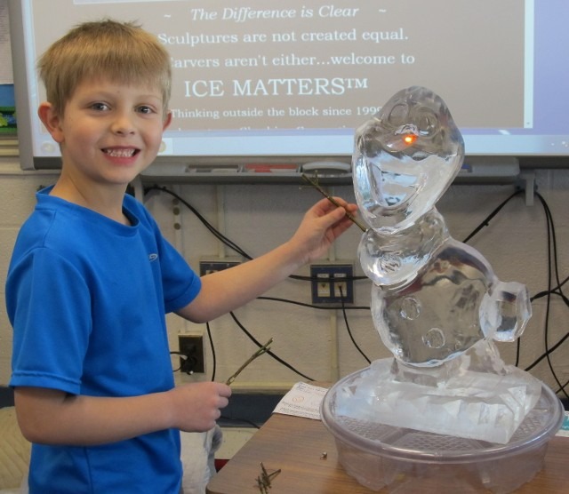 Smiling young boy pointing at a custom clear ice sculpture display