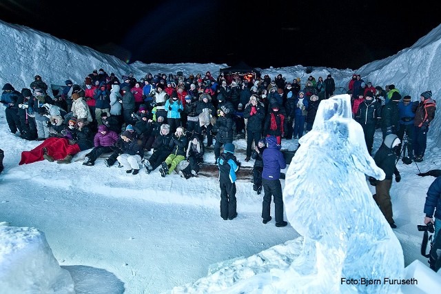 A large crowd gathered around an outdoor winter festival ice carving stage