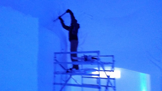 Silhouette of an artist carving a massive ice wall from scaffolding under blue light