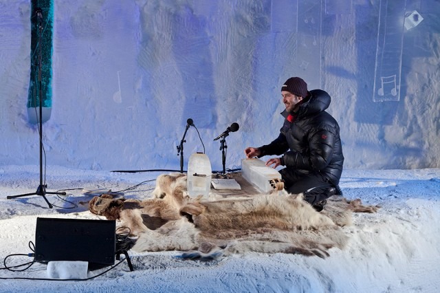 Musicians performing live with acoustic instruments inside a carved ice studio